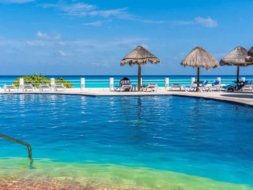 Sparkling beachfront pool ringed by palapas above the glowing Caribbean, sun and sea at your fingertips