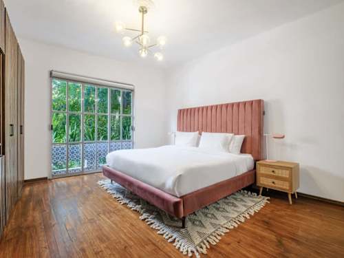 Serene bedroom with a blush upholstered bed and leafy window views for a great night's sleep