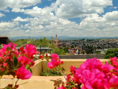 Rooftop framed by vivid bougainvillea with the town skyline and church domes beyond, classic San Miguel charm