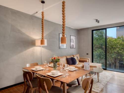 Bright dining area under sculptural pendants beside tall windows, a warm setting for a long, easy dinner in