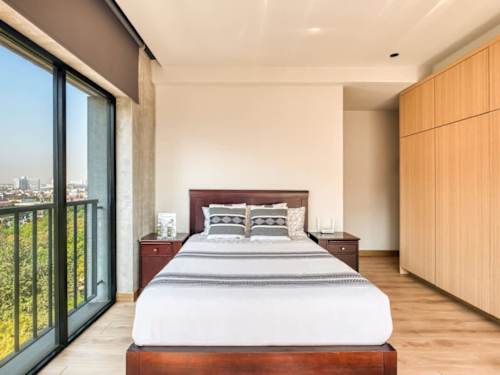Airy bedroom with a comfy bed and full height glass, natural light pouring in over the downtown rooftops