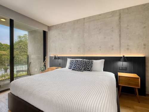 Restful king bedroom with a concrete-chic headboard and leafy window view, a calm retreat near Parque Mexico