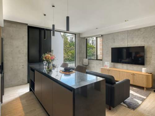 Open living and kitchen space with an island, TV and warm concrete walls, relaxed and design-forward