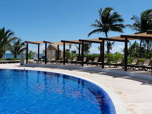 Expansive resort pool with a shaded pergola and swaying palms, your daily escape beside the Caribbean
