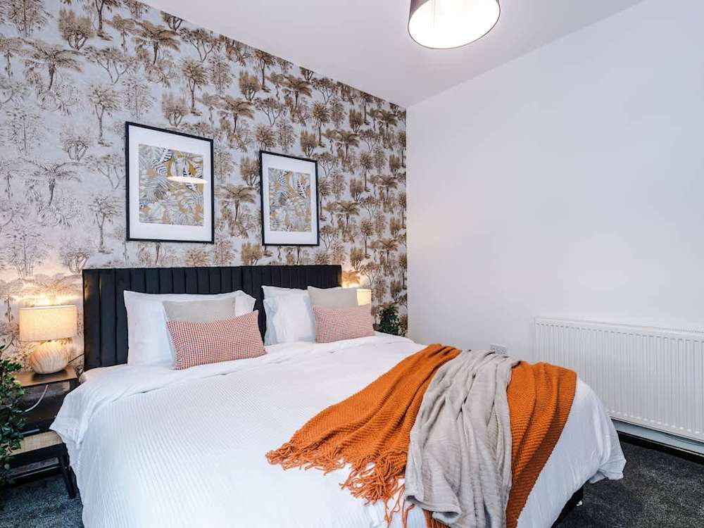 Bedroom in the same Alpha Street house, with a double bed, upholstered headboard and bedside lamps.