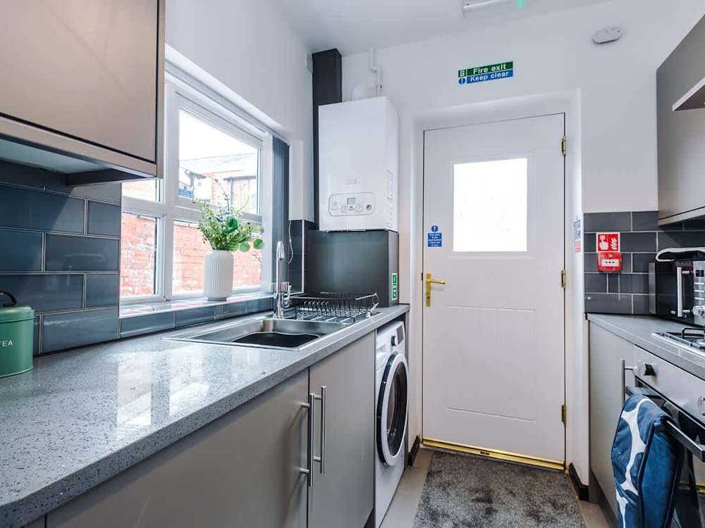 Galley kitchen in the same Alpha Street house, with a washing machine, oven and a window over the sink.