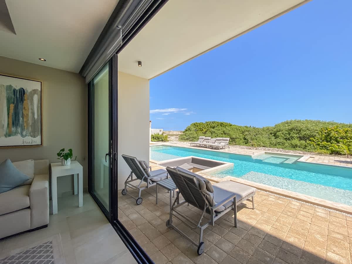 Private terrace with sweeping pool and Caribbean views, sliding glass doors that blur the line between indoors and the Isla Mujeres coast