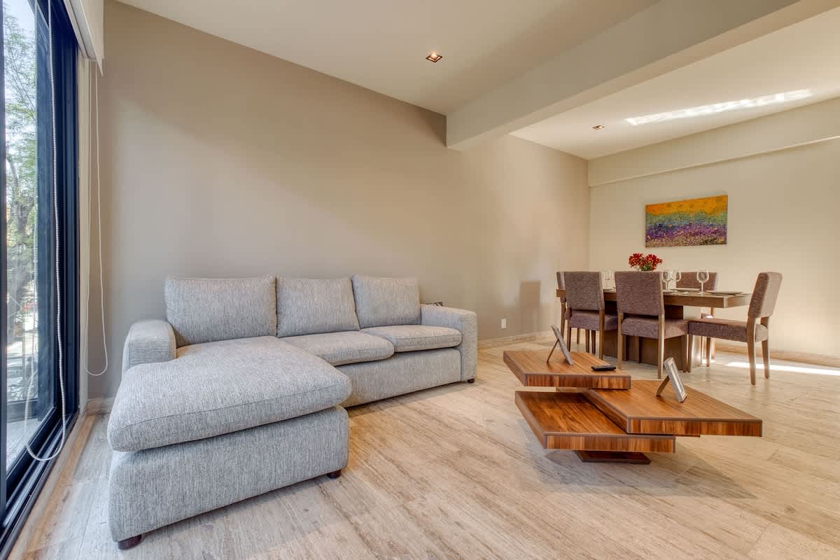 Open-plan living and dining area with a plush sofa and warm wood floors, easy, bright living in the heart of Roma Norte