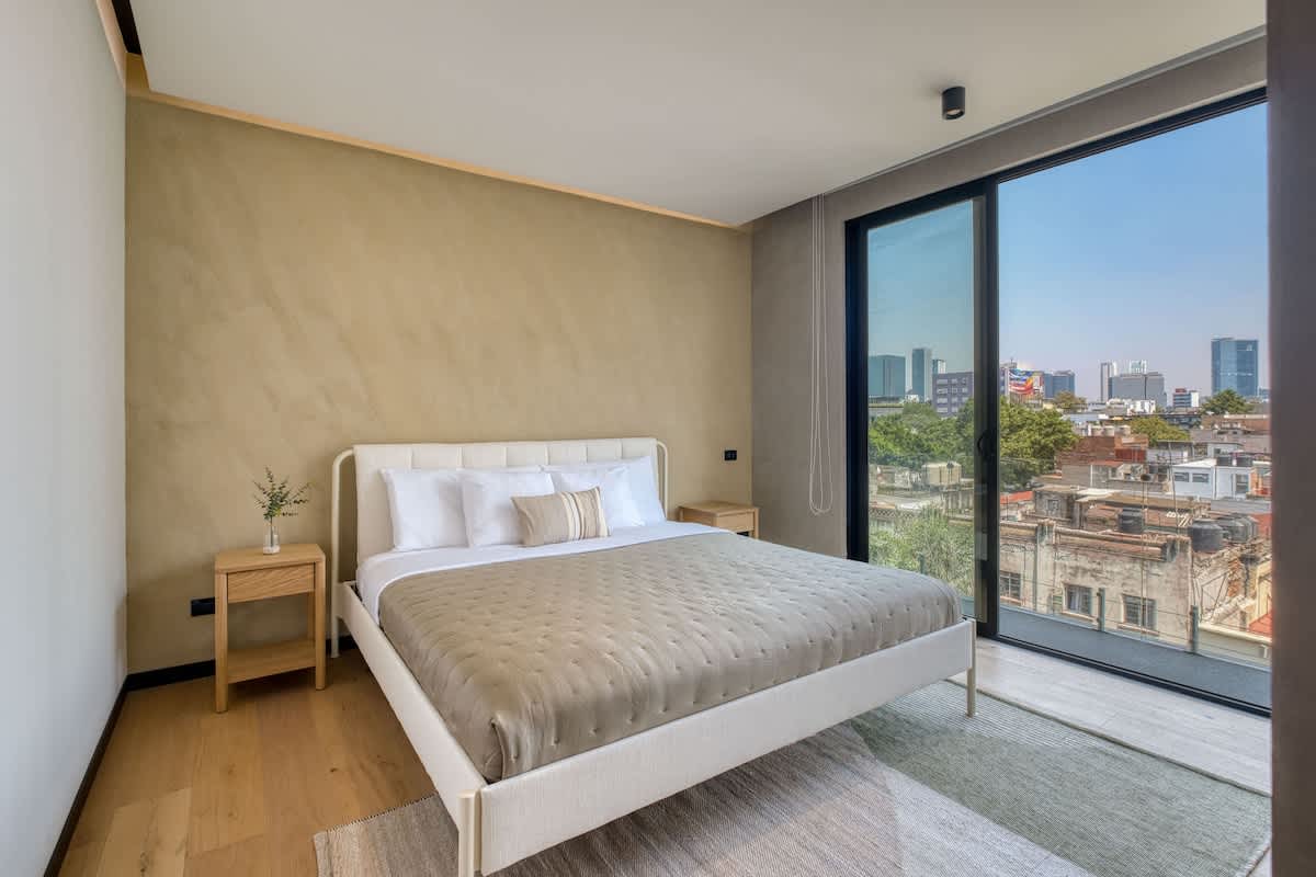 Restful bedroom with a comfy queen bed and floor-to-ceiling windows framing Roma Norte, wake to light and city views