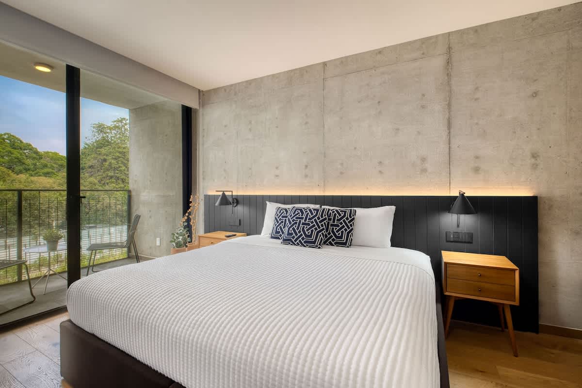 Restful king bedroom with a concrete-chic headboard and leafy window view, a calm retreat near Parque Mexico