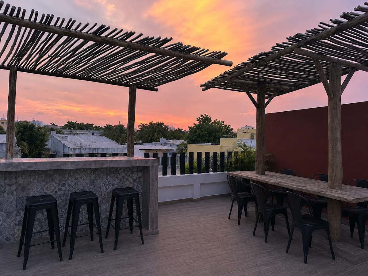 Shared rooftop bar under a rustic pergola glowing at sunset, unwind with a cocktail above downtown Cancun near Mercado 28