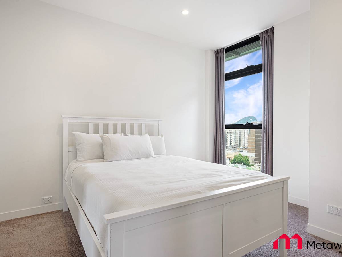 Bedroom featuring a queen-size bed, bedside table, and natural light.