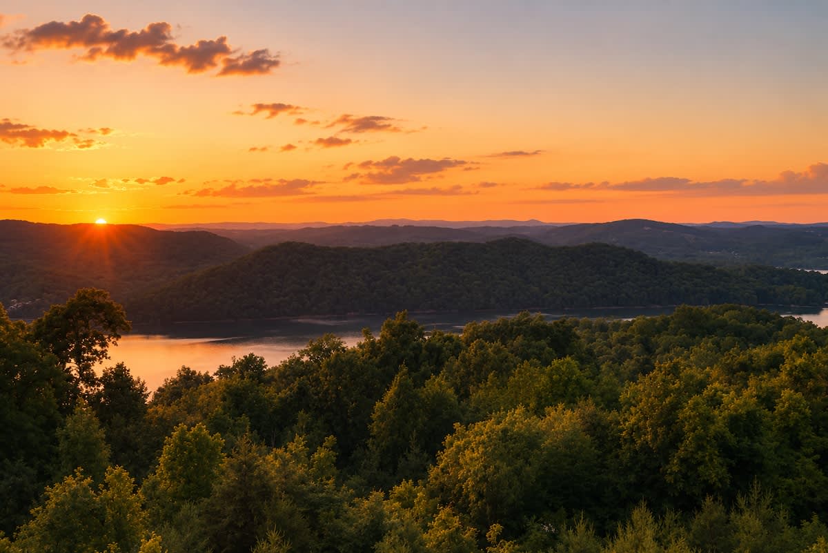 The sun setting orange over Norris Lake and forested hills, seen from the cabin