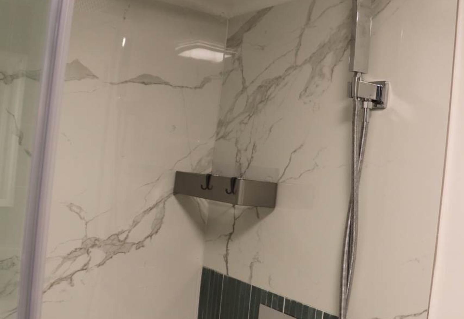 Indulge in a spa-like experience with this beautifully renovated walk-in shower, featuring elegant marble-look tile, rainfall showerhead, matte black fixtures, and modern coastal design.
