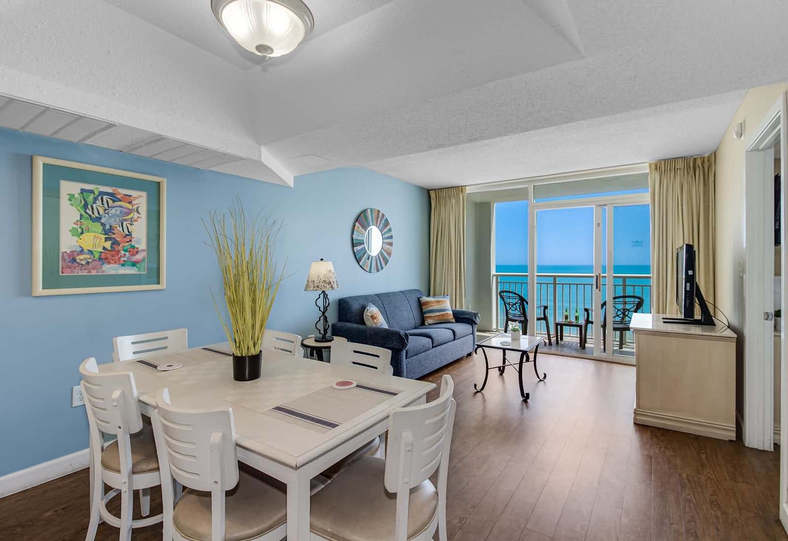 Gather and unwind in this inviting dining and living area with vibrant décor, ample seating, and breathtaking ocean views from the private balcony. Perfect for shared meals and relaxation—your coastal escape awaits. 