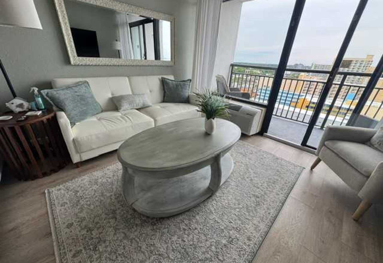 Bright and inviting seating area with a plush white sofa, decorative mirror, and scenic views
