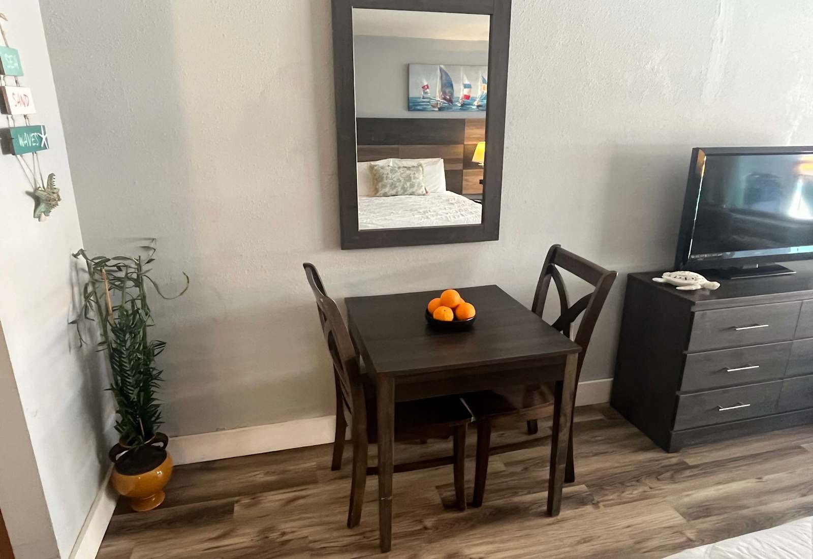 Intimate dining area featuring a dark wood table with two chairs, a decorative bowl of oranges, and a wall-mounted mirror reflecting the studio space.
