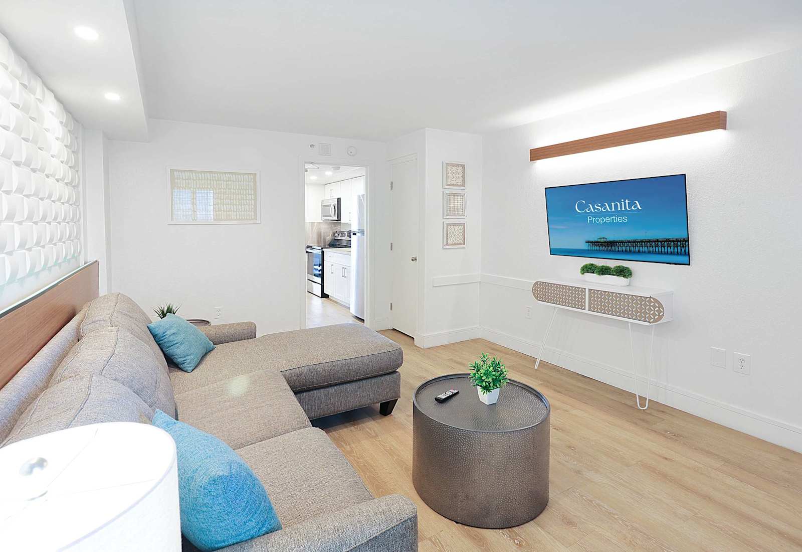 Relax in this inviting living space featuring a plush sectional sofa, wall-mounted TV, and modern decor. Perfect for unwinding after a day at the beach, this cozy area offers comfort and style, with easy access to the kitchen and bedroom.