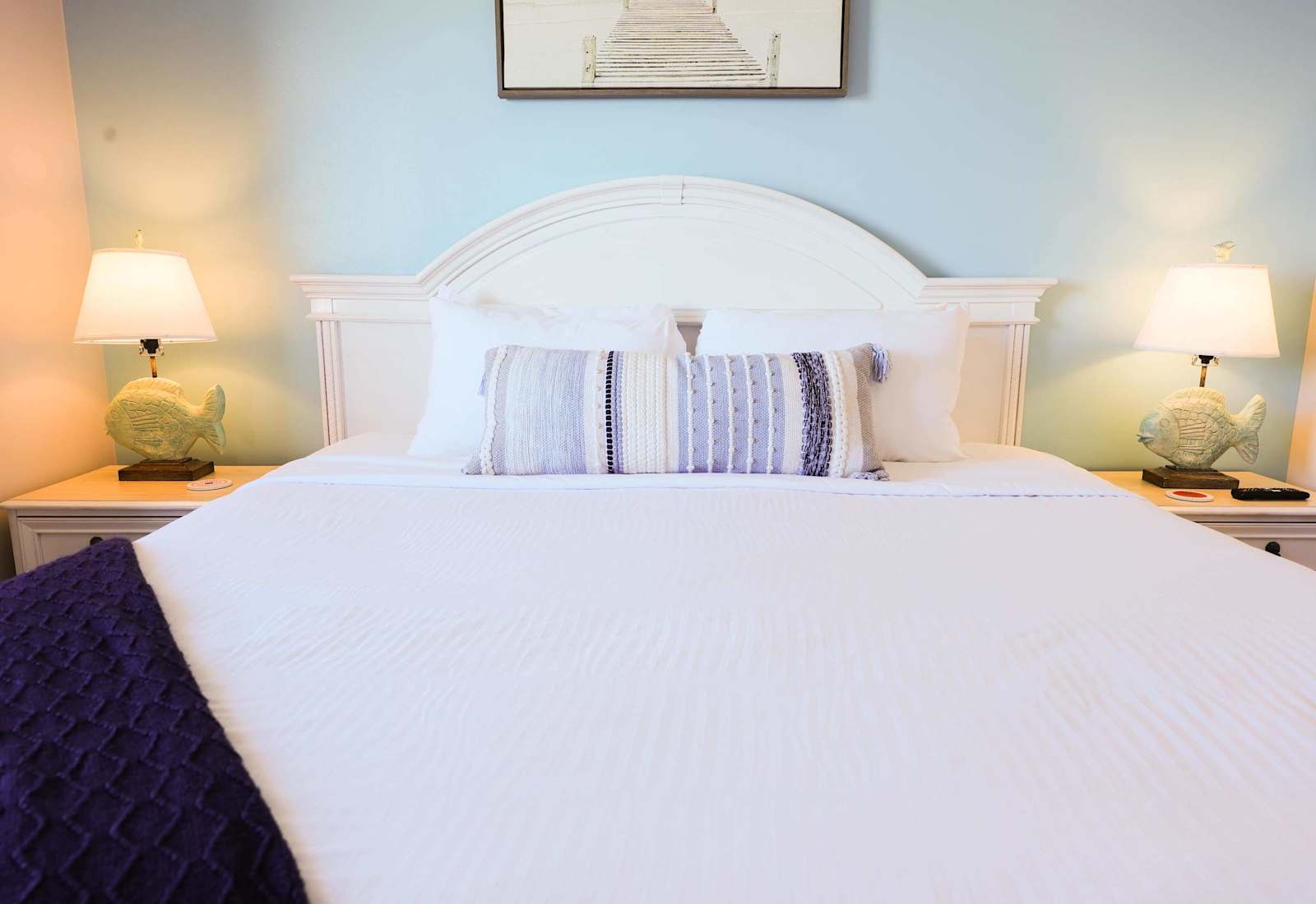 Bright and coastal bedroom retreat with a king-sized bed, soothing blue walls, and charming fish-shaped lamps — perfect for a relaxing beach getaway!