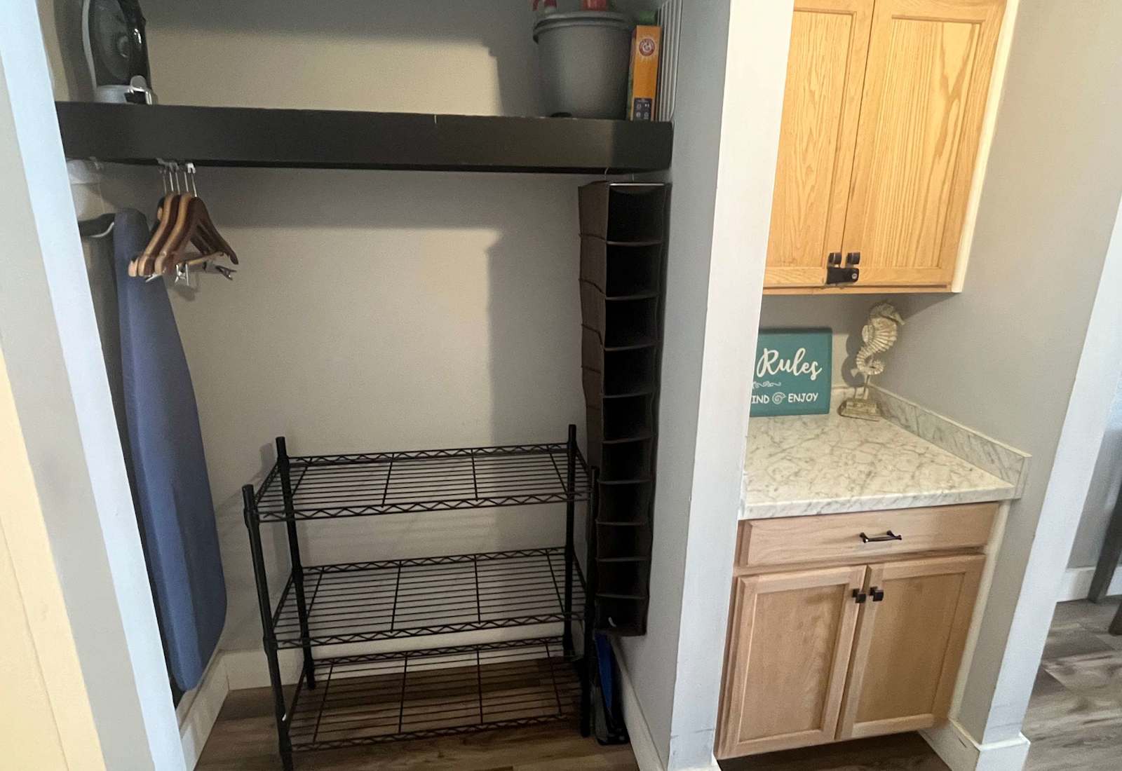 Functional closet and storage nook equipped with wire shelving, hanging organizers, an iron, an ironing board, and a built-in cabinet station.