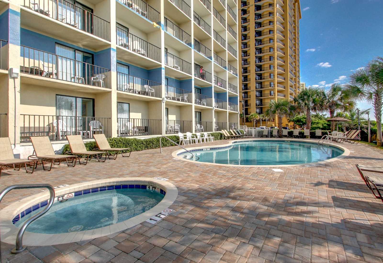 Resort pool area with lounge chairs, palm trees, and a nearby hot tub for relaxing between beach outings.