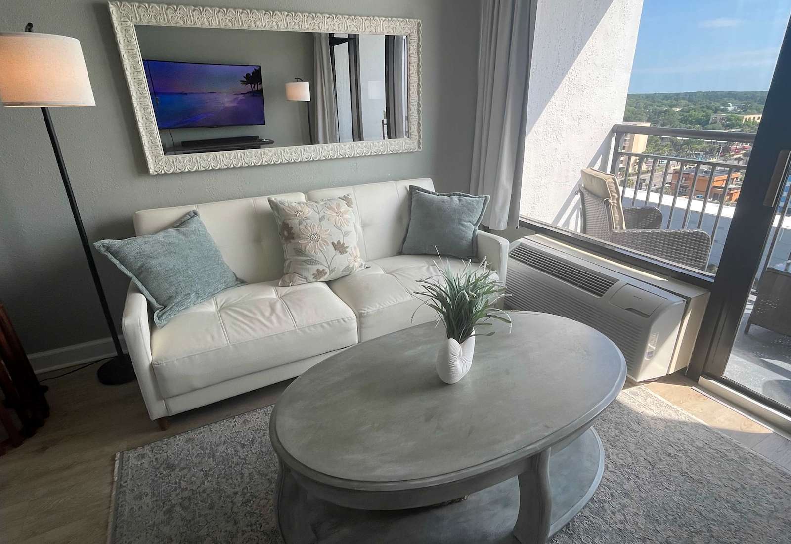 Bright and inviting seating area with a plush white sofa, decorative mirror, and scenic views