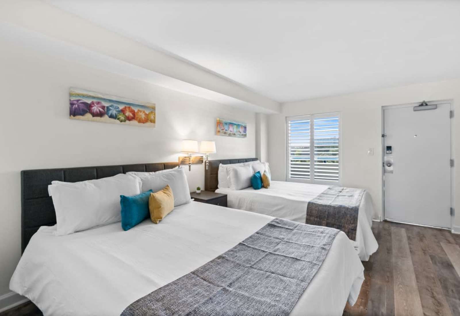 Bright and inviting, this coastal-inspired bedroom features two plush beds, soft linens, and vibrant décor—perfect for families or friends looking to relax and recharge after a sun-soaked day at the beach.
