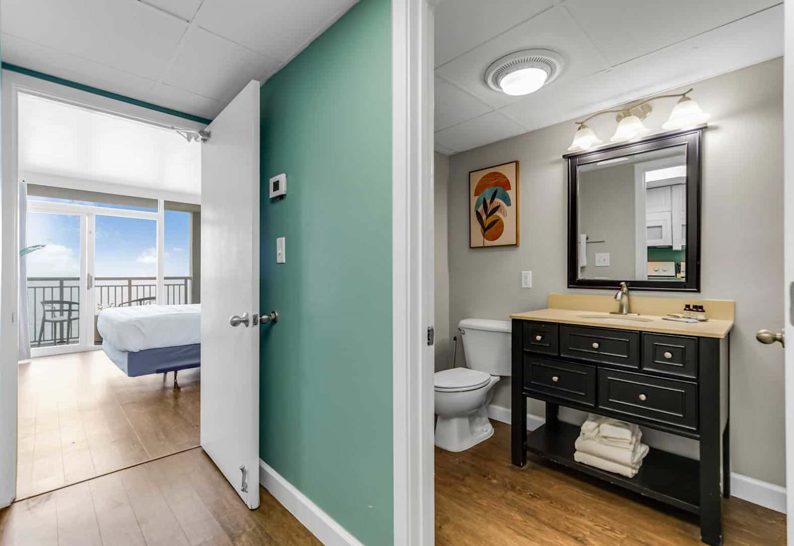 Step into this elegant bathroom featuring a modern vanity, warm lighting, and thoughtful details. With direct access to your cozy bedroom and balcony views, convenience meets coastal charm for a seamless stay.