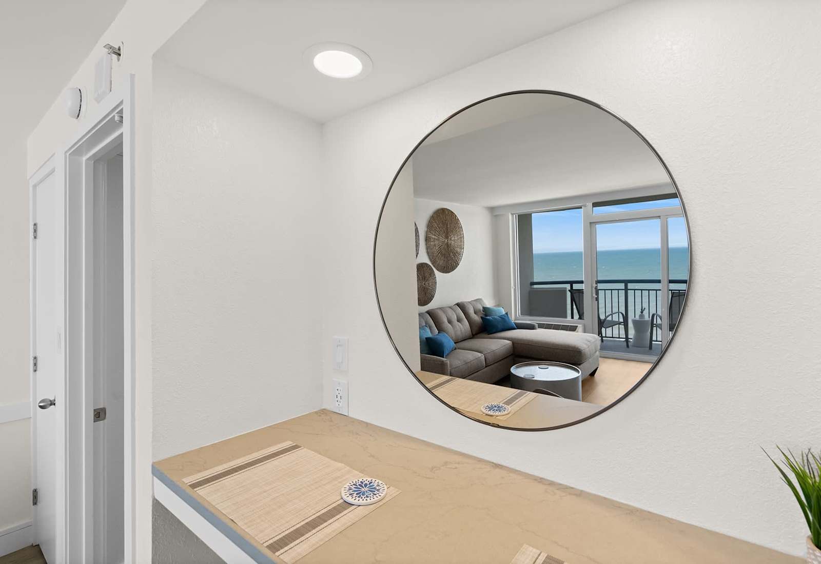  Step into a stylish and inviting space. A large circular mirror reflects the stunning ocean views and cozy living area, setting the tone for a relaxing beach getaway.