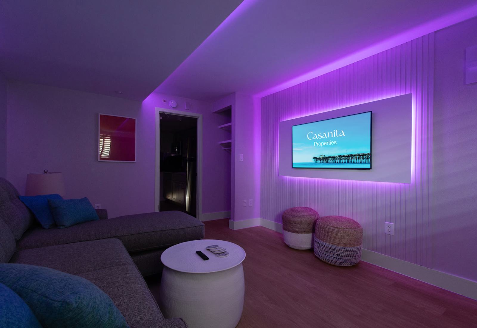 Enhanced by ambient purple lighting that sets a relaxing mood. The cozy sectional, modern decor, and wall-mounted TV create an inviting atmosphere, perfect for evening relaxation or movie nights in style.