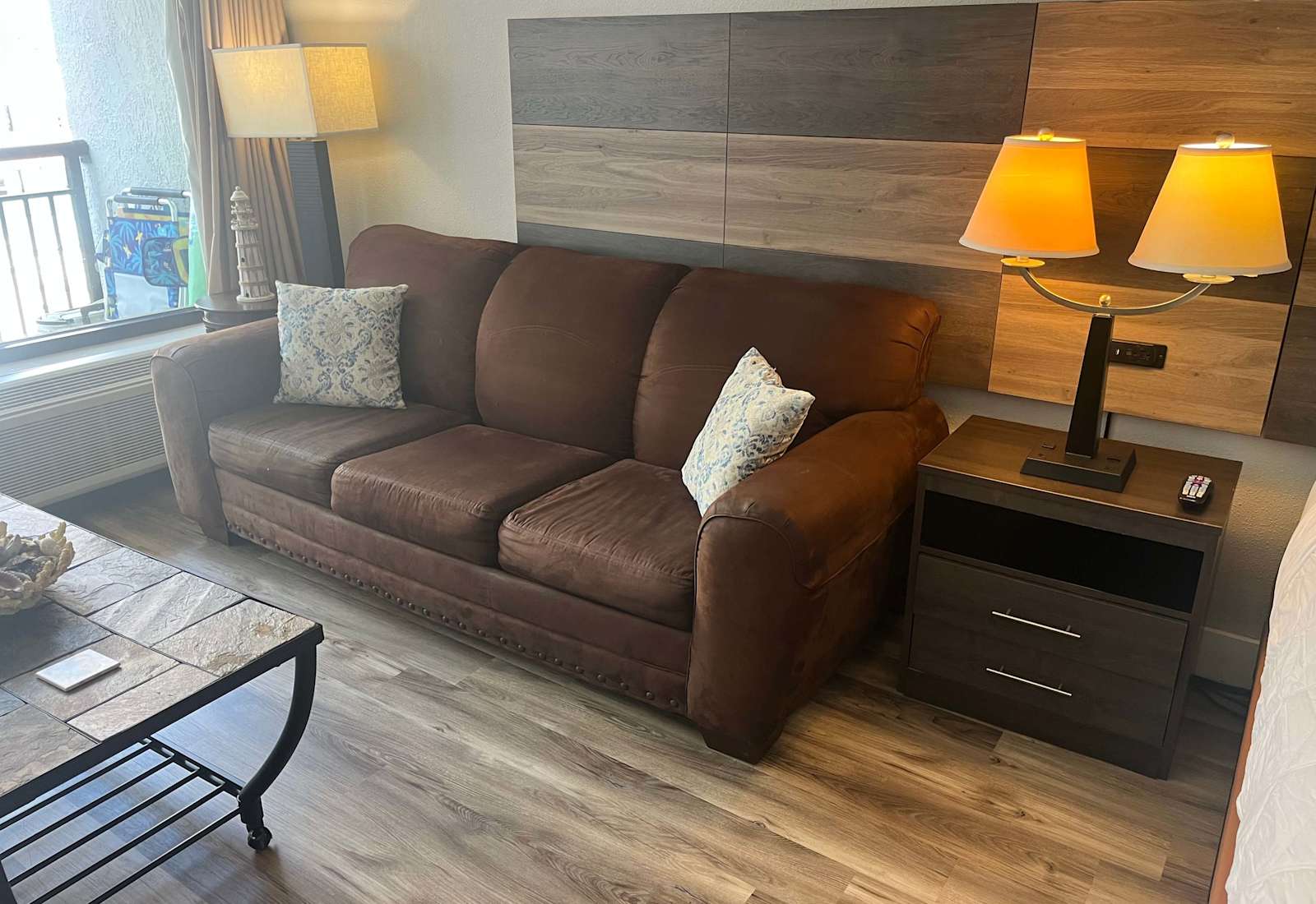 Cozy living area featuring a comfortable brown sofa, matching pillows, a wood-accented wall panel, and modern lighting.