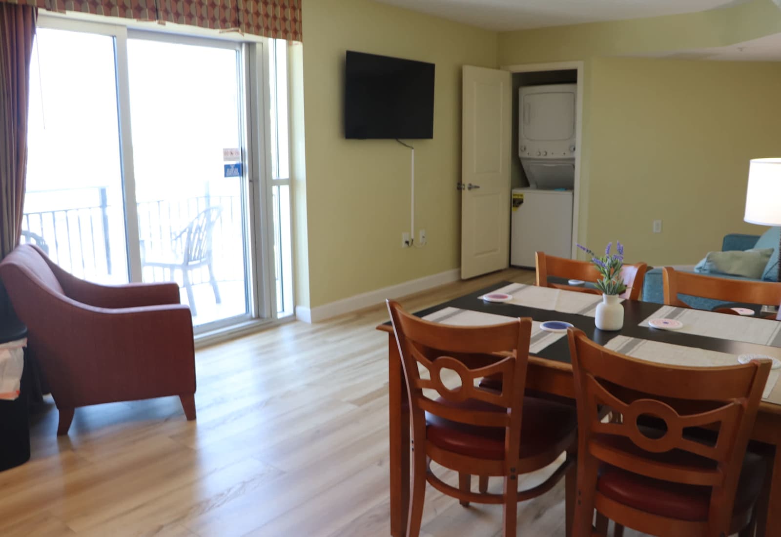 Comfortable dining and living area with balcony access, a wall-mounted TV, and in-unit laundry nearby — a convenient space to relax, dine, and enjoy your Myrtle Beach stay.