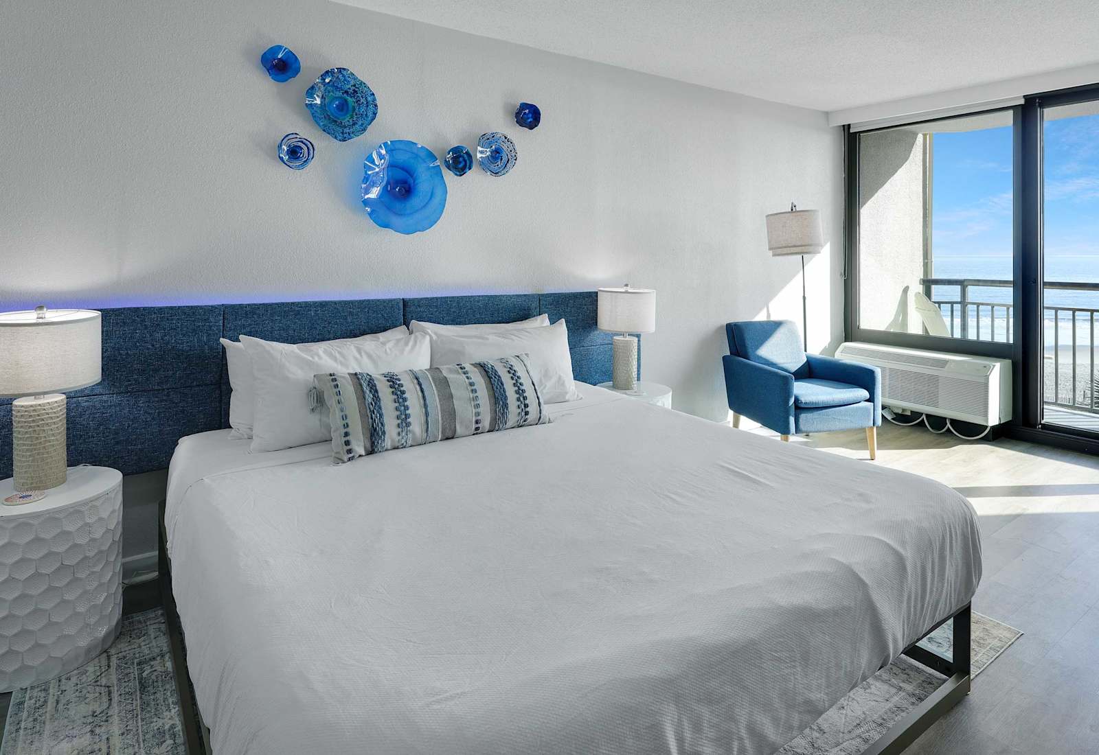 Bright ocean-view sleeping area with a comfortable king bed, coastal-blue accents, and private balcony access for a relaxing Myrtle Beach stay.