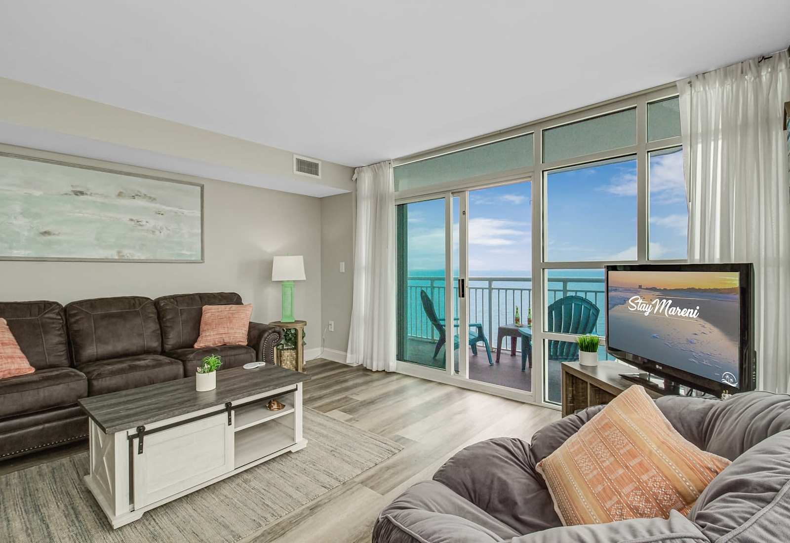 Inviting living room with cozy seating, a TV, and floor-to-ceiling windows opening to a private balcony with ocean views.