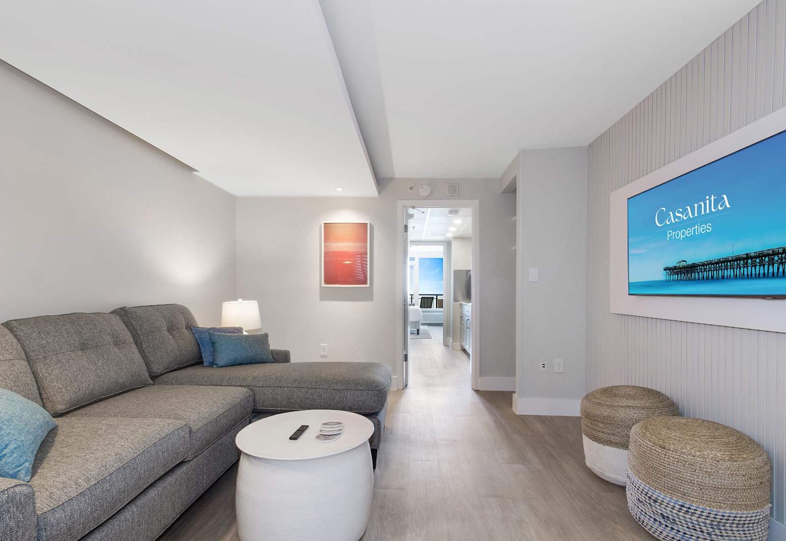 Relax in this inviting living space featuring a plush sectional sofa, wall-mounted TV, and modern decor. Perfect for unwinding after a day at the beach, this cozy area offers comfort and style, with easy access to the kitchen and bedroom.