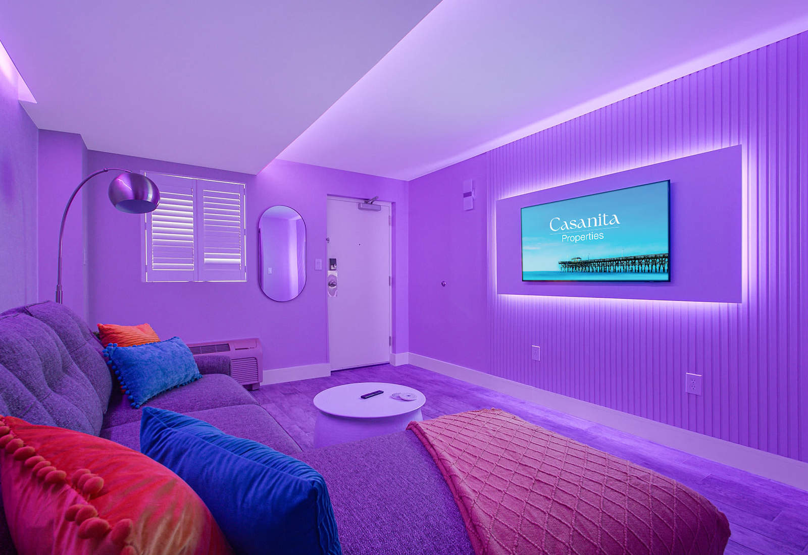 Enhanced by ambient purple lighting that sets a relaxing mood. The cozy sectional, modern decor, and wall-mounted TV create an inviting atmosphere, perfect for evening relaxation or movie nights in style.