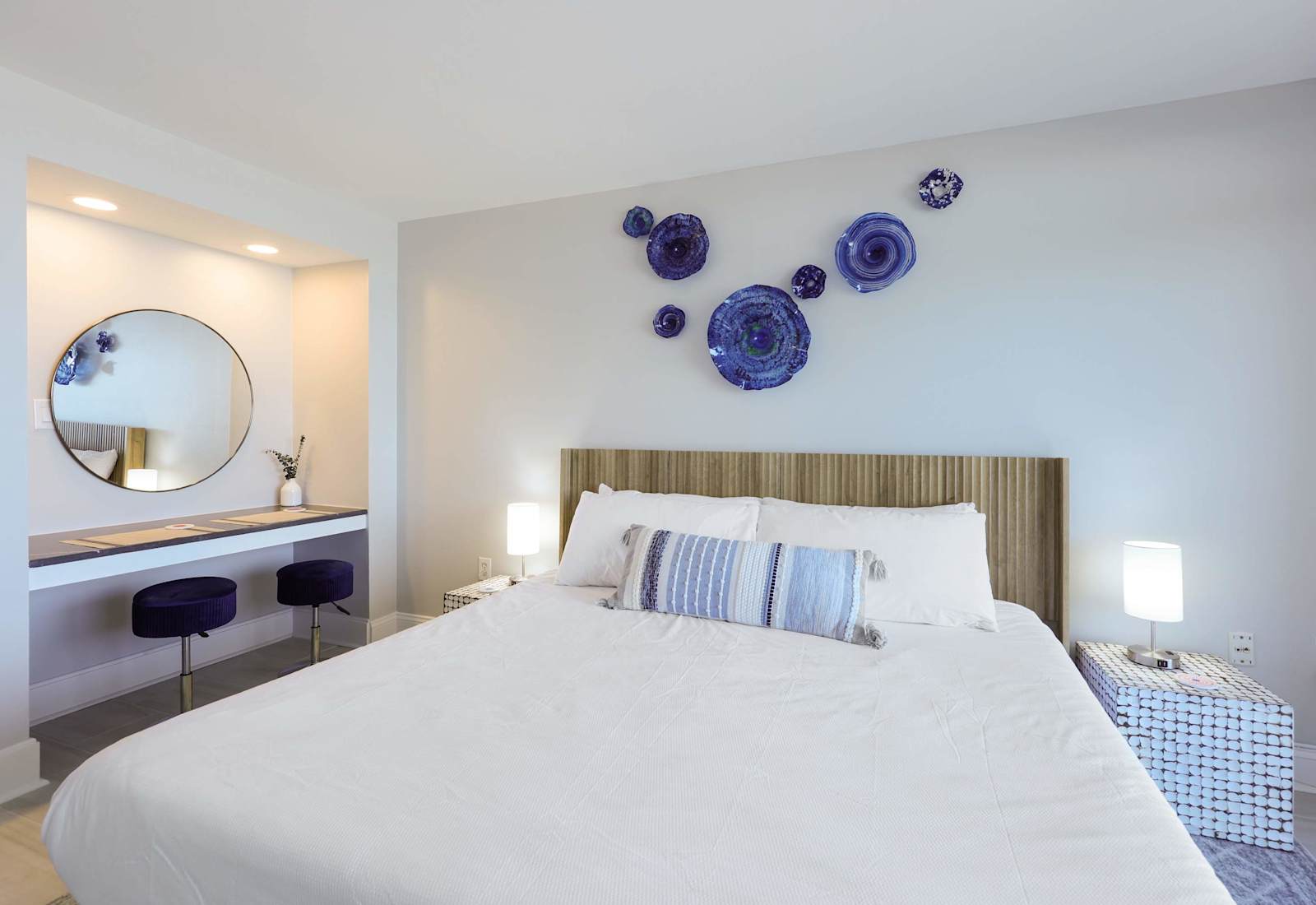 Drift off in this dreamy coastal bedroom featuring bold blue art, a plush king bed, and a stylish vanity nook—perfect for relaxing after a day at the beach. Coastal comfort meets modern charm in every detail.