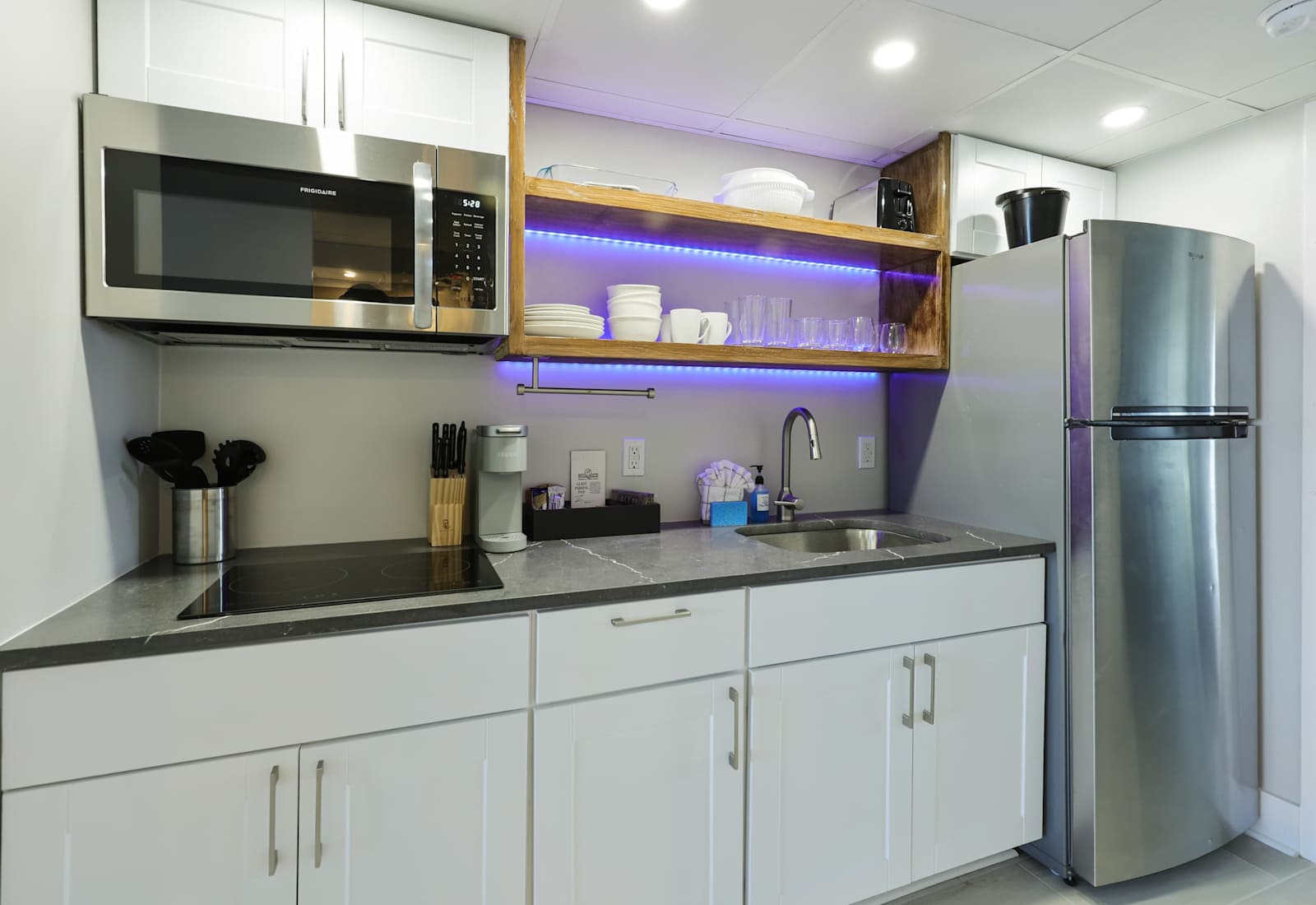 Whip up vacation meals with ease in this sleek, fully stocked kitchenette—complete with stainless steel appliances, open shelving, and a pop of ambient lighting for those cozy, late-night snacks by the beach.