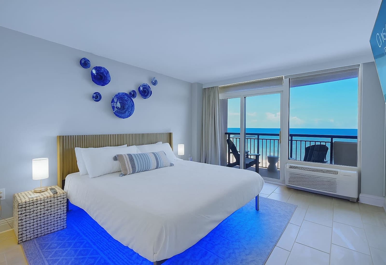 Wake up to oceanfront views and unwind in this modern coastal retreat featuring a glowing underlit king bed, private balcony, and relaxing sea breeze—perfect for your next beachfront escape.