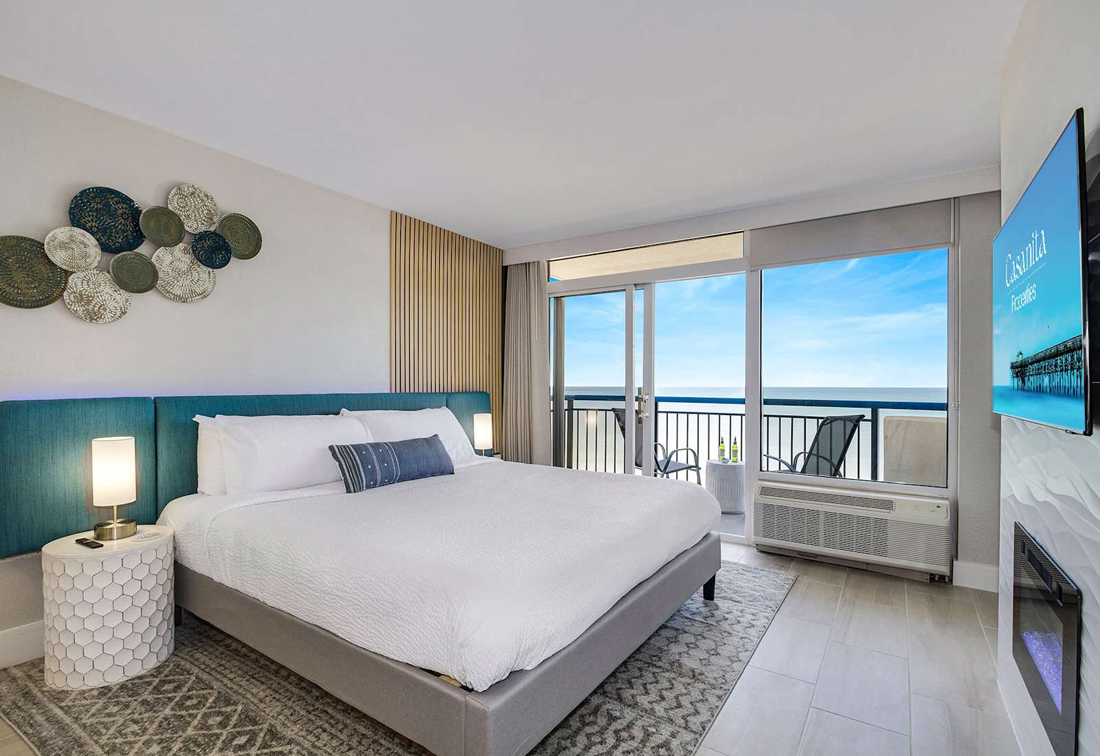 Wake up to serene ocean views in this stylish bedroom with floor-to-ceiling windows and a private balcony. Enjoy natural light, a cozy bed, modern fireplace, and sleek TV, blending comfort and luxury. Perfect for a relaxing retreat by the sea.