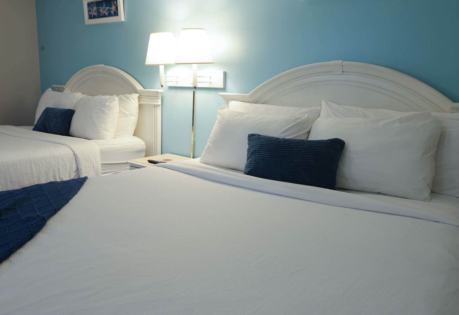 Cozy coastal guest room featuring two plush queen beds with crisp white linens, soft blue accents, and tranquil beach-inspired decor — ideal for families or friends.