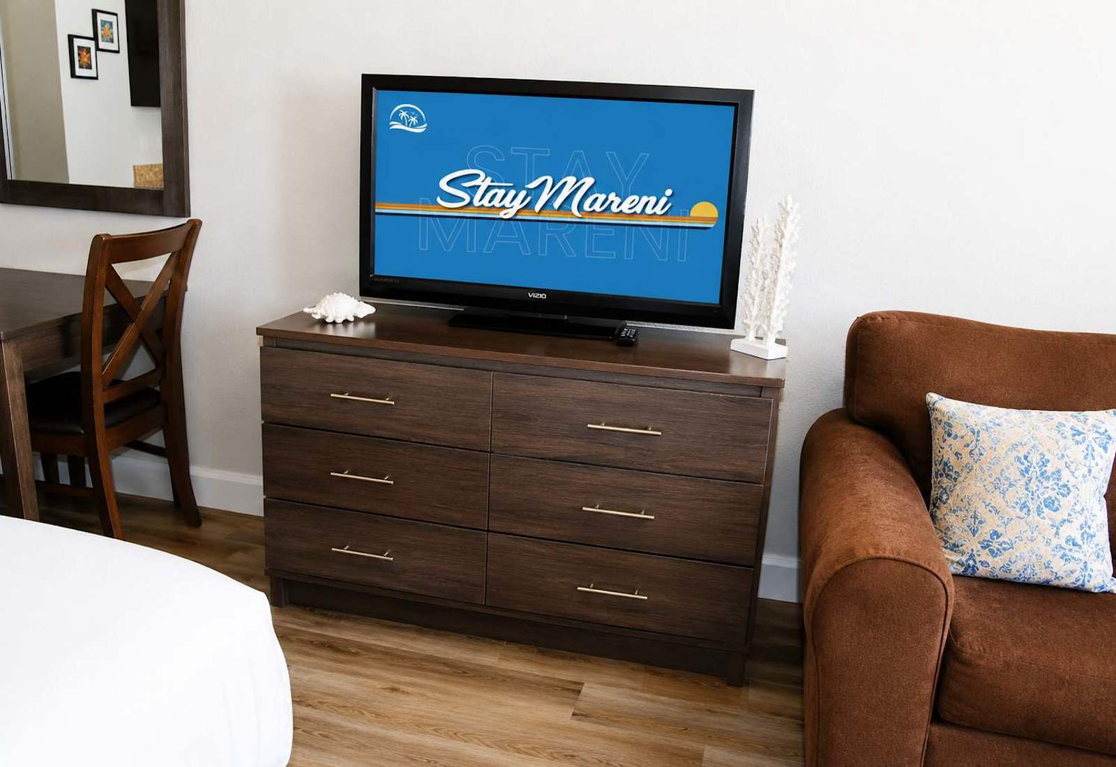 Modern gray wood-finish six-drawer dresser supporting a flat-screen television, flanked by coastal decor accents.