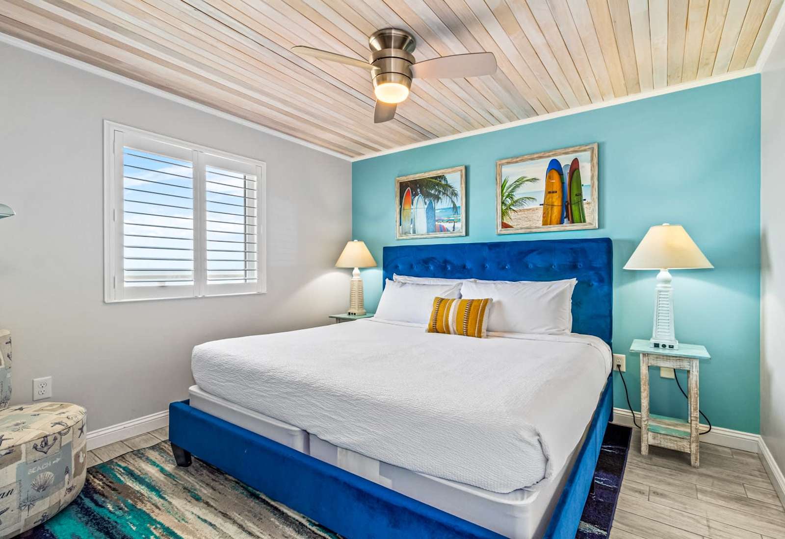 Unwind in this cozy bedroom featuring a plush king-sized bed, nautical-inspired decor, and a ceiling fan for added comfort. Wake up refreshed with natural light and glimpses of the ocean just outside your window—your perfect seaside retreat!