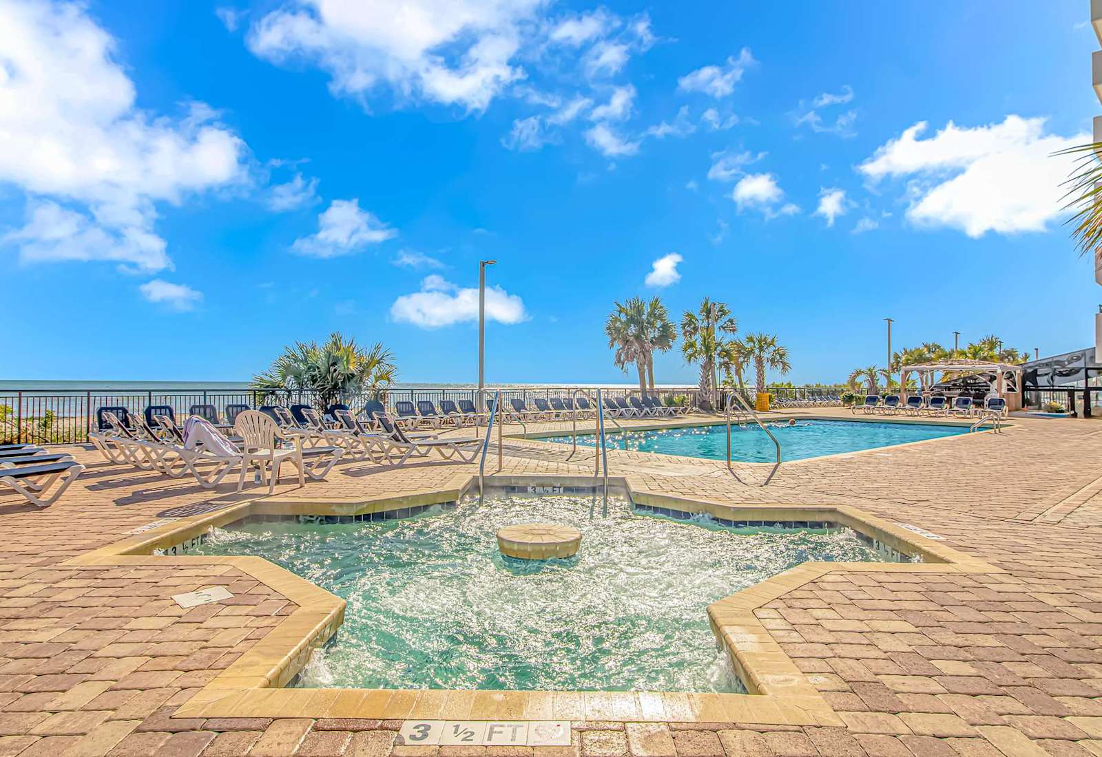 Outdoor pool and spa area with lounge seating, palm trees, and ocean views for a relaxing Myrtle Beach getaway.