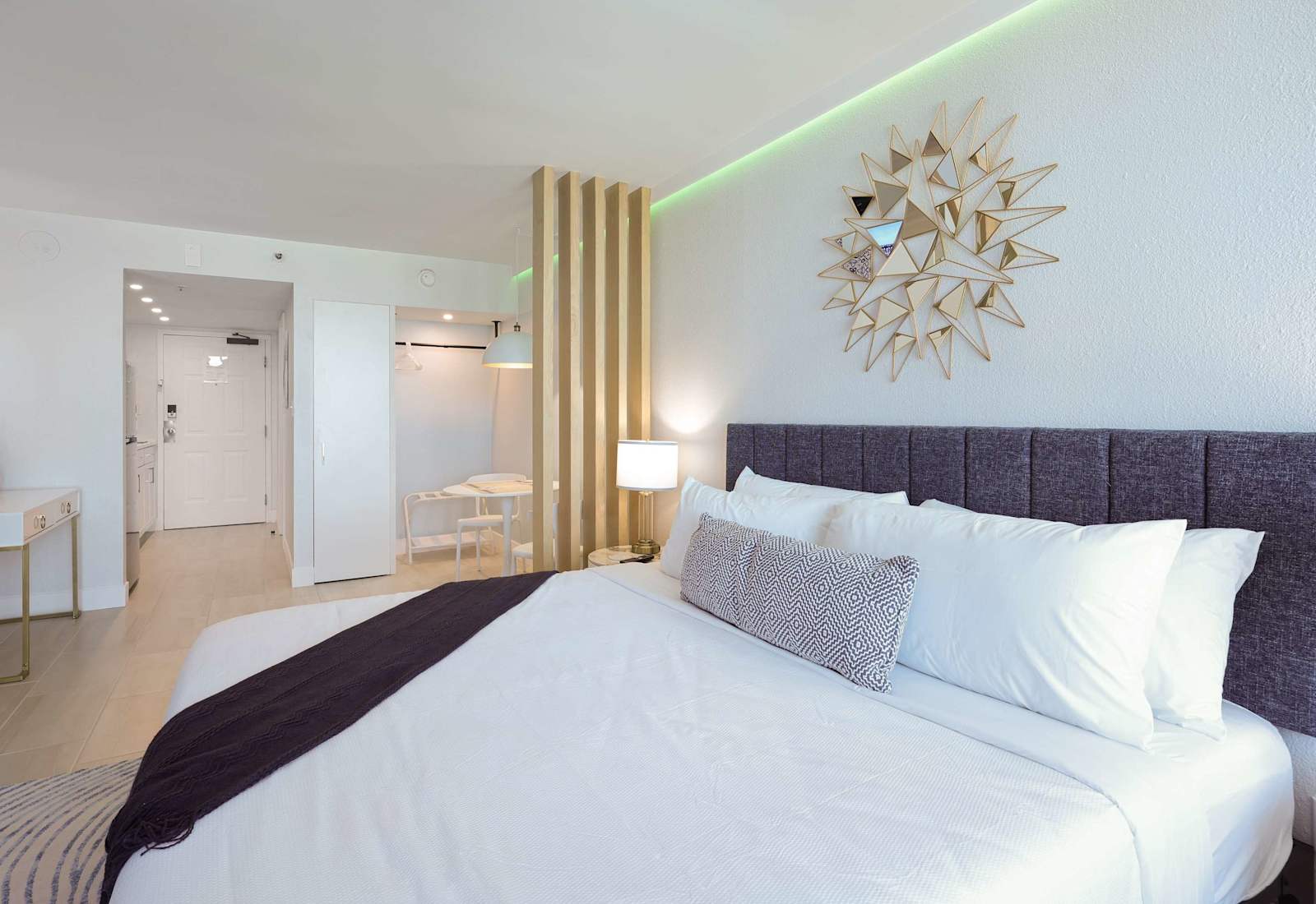 This elegant studio suite is a masterclass in modern coastal comfort. The plush king-size bed, dressed in crisp white linens and accented with a textured navy throw and geometric lumbar pillow, promises restful nights in style.