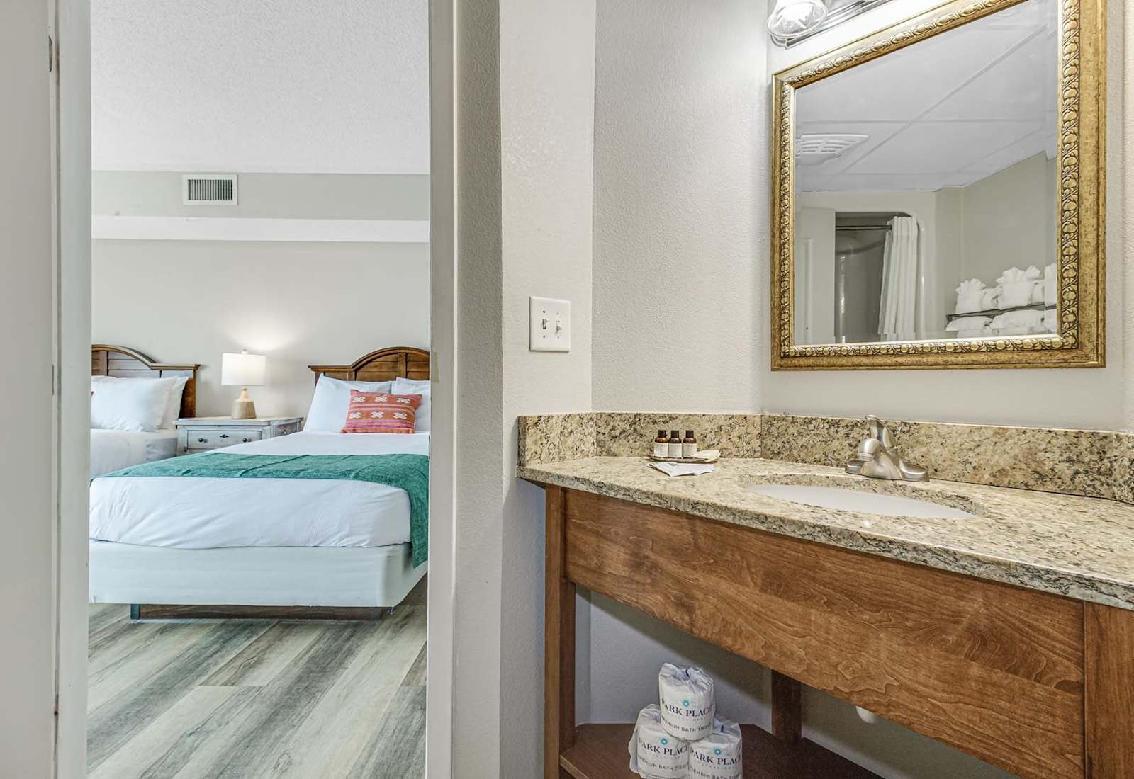 Bathroom vanity with granite countertop, framed mirror, fresh towels, and easy access from the nearby bedroom.