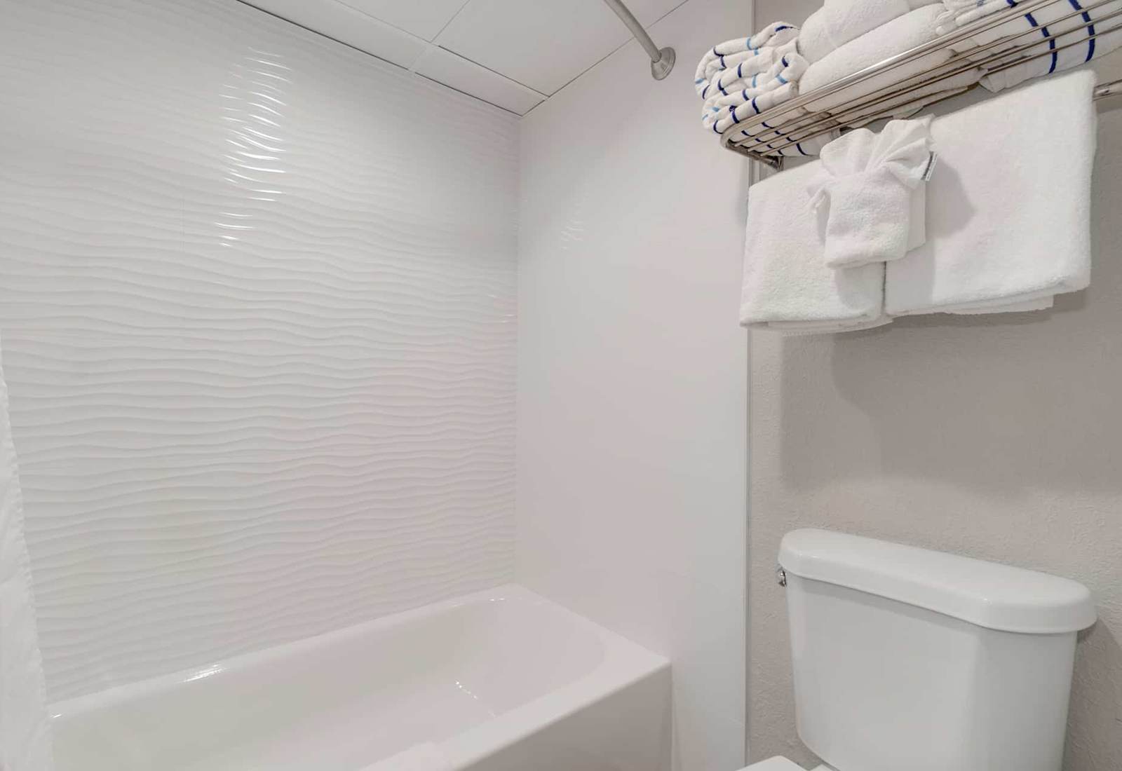 Refresh in this spotless bathroom featuring a wave-textured wall, sleek tub, and plush towels.