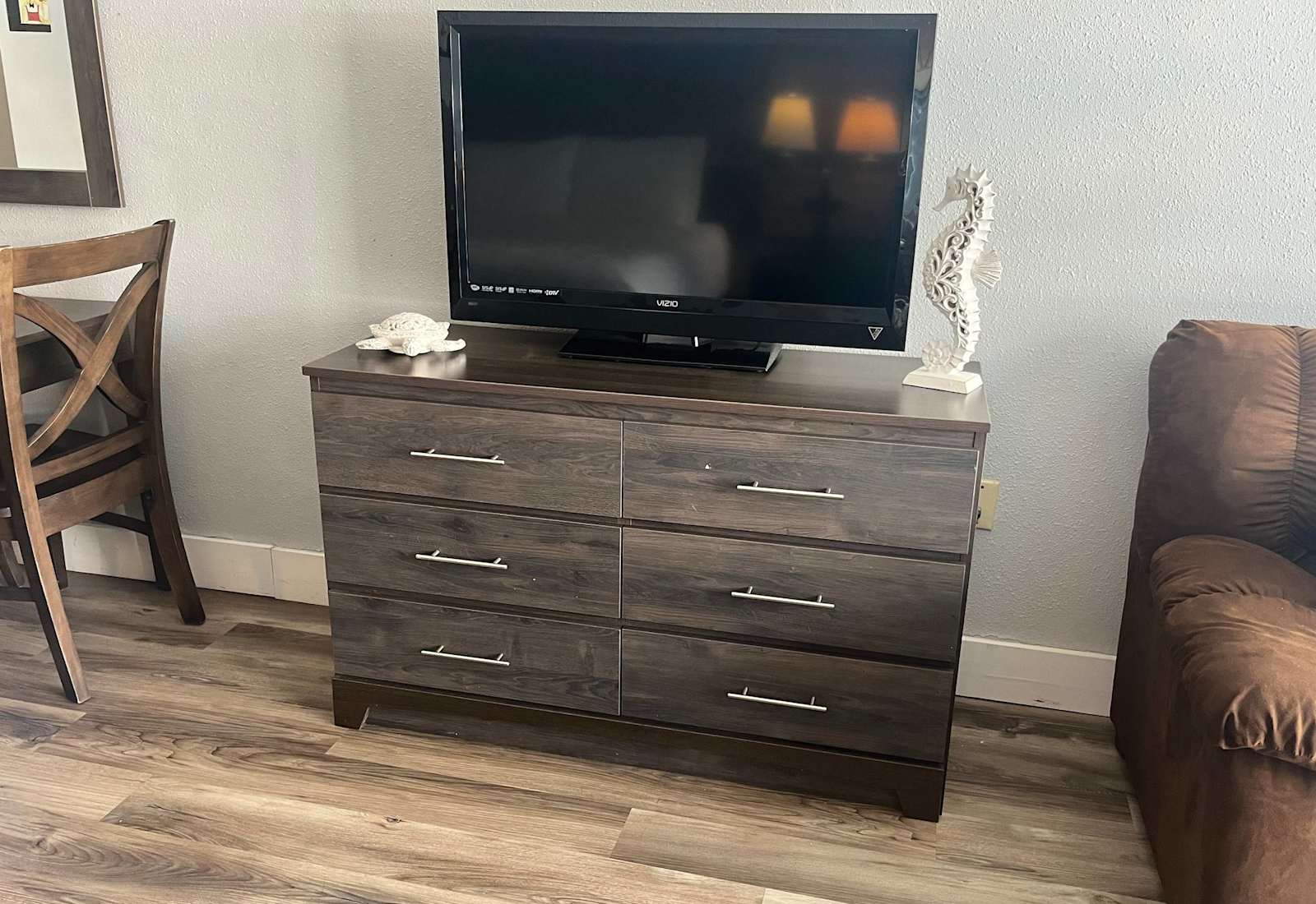 Modern gray wood-finish six-drawer dresser supporting a flat-screen television, flanked by coastal decor accents.