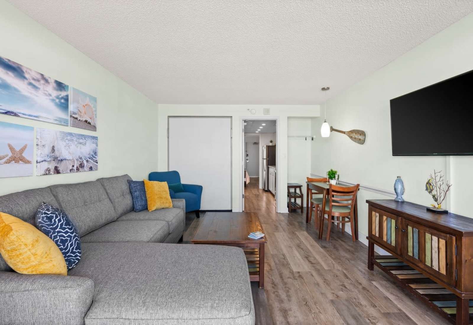 Spacious and stylish living area featuring a cozy sectional, coastal décor, and smart TV—perfect for relaxing after a day at the beach or enjoying meals in the adjoining dining nook.