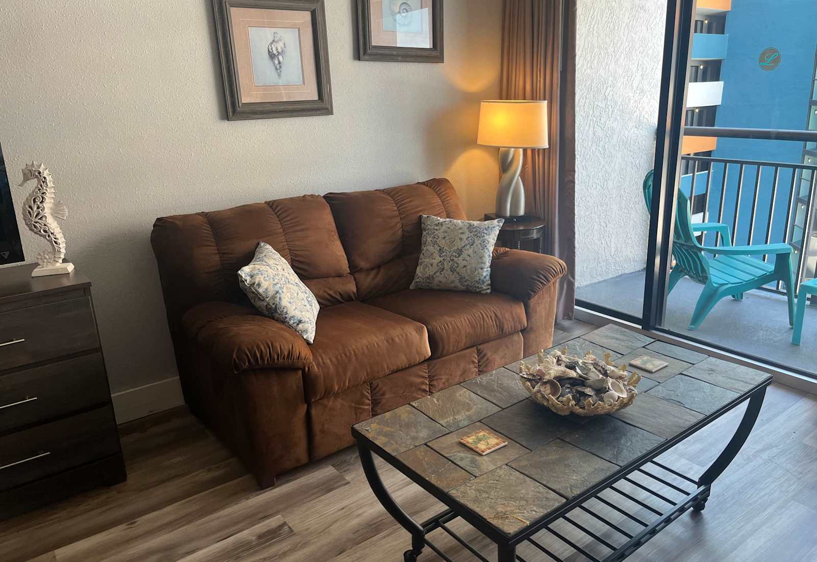 Cozy seating area featuring a comfortable brown love seat with patterned pillows, a tile-top coffee table, and large sliding glass doors leading out to a private balcony.